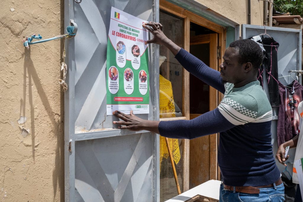 a man pinning up a cornavirus information poster fact sheet on a door in Africa