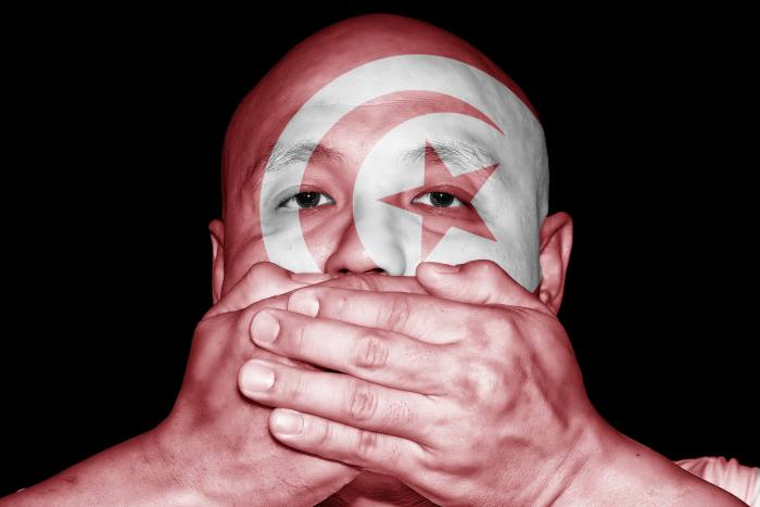 bald man with the tunisian flag painted on his face covers his mouth