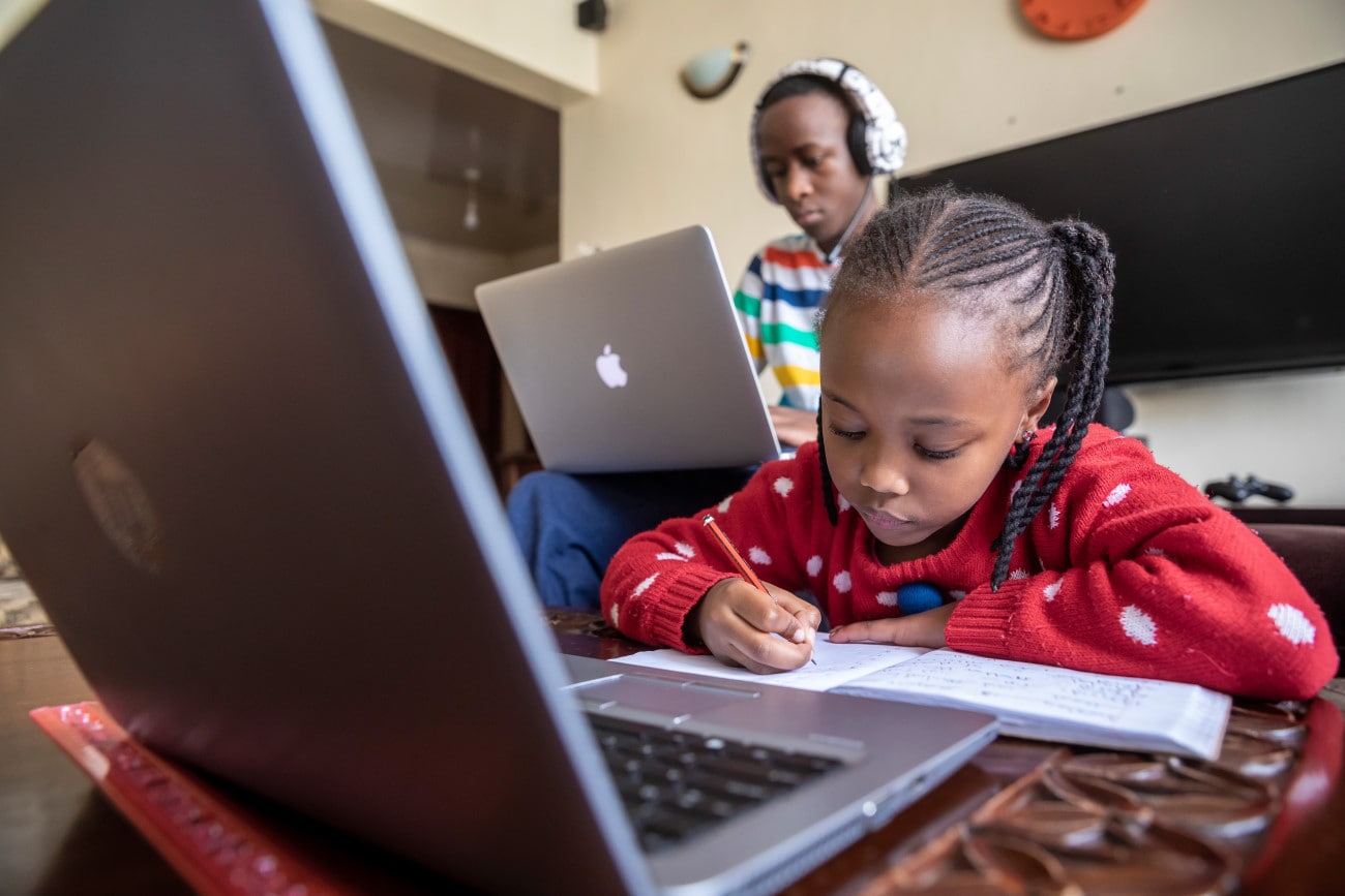 A young girl works with a laptop with her mother sitting behind her