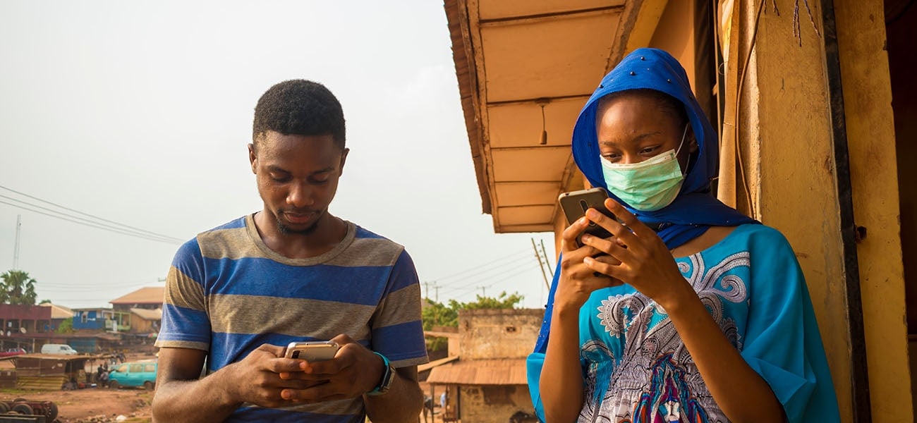 A man and a woman in Africa one wearing a face mask look at their phones