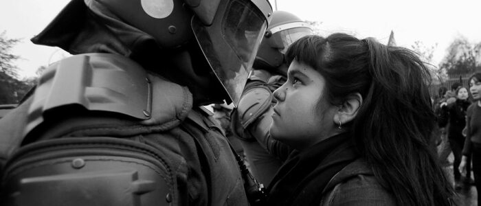 young protestor standing face to face with riot police wearing full riot gear protection