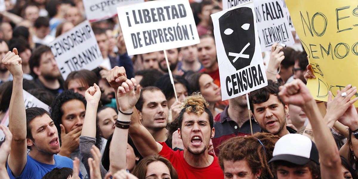 Protestors in Spain holding up banners and placards for freedom of expression