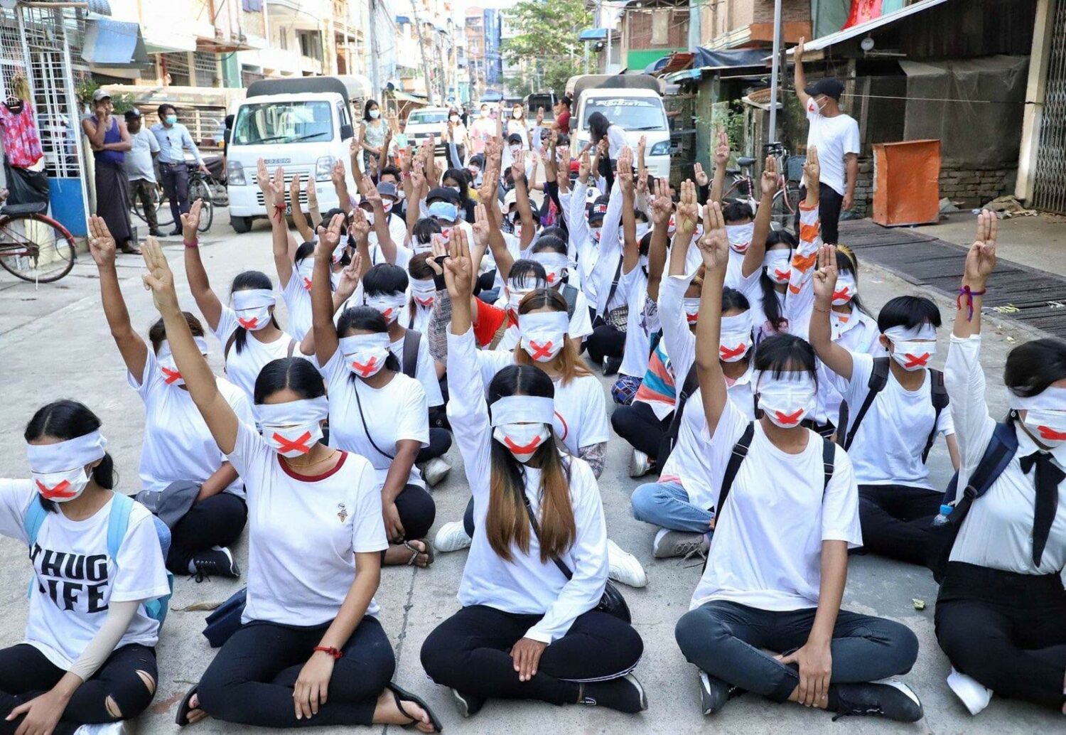 A group of protestors in Myanmar sit cross legged with a mask covering their eyes